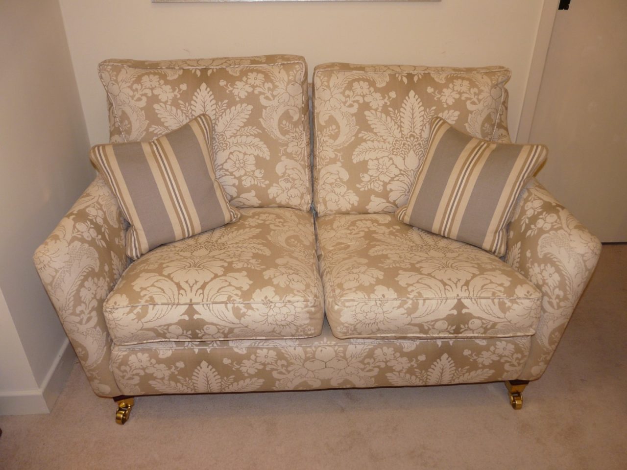 Small 2 seater sofa, low arms, wooden feet, contrasting scatters.